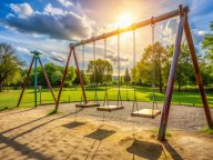A vacant swing set stands ready at a sunny playground, awaiting
