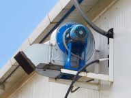 The air exhaust system is installed outside the building. Electrical equipment for extracting and filtering air. Blue electric motor with an air duct on the wall of the building. Selective focus