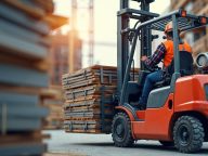 Forklift operator transports construction materials. Worker drives vehicle. Man wearing safety helmet, vest. Loading unloading process. Organized logistic at building site. Transportation of wooden