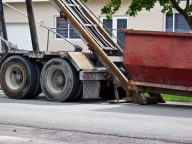 Empty roll-off construction dumpster being unloaded from truck a
