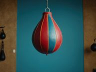 A red and blue boxing bag suspended from a ceiling, ready for use